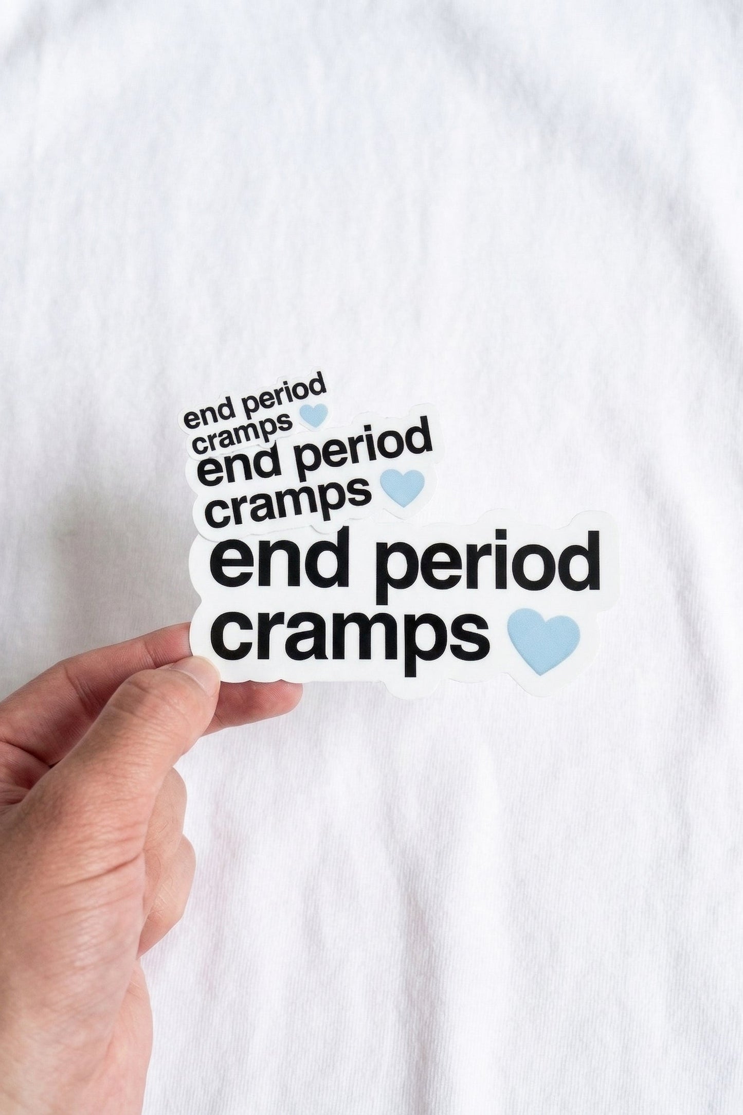 Hand holding a sticker with 'end period cramps' text on a white background