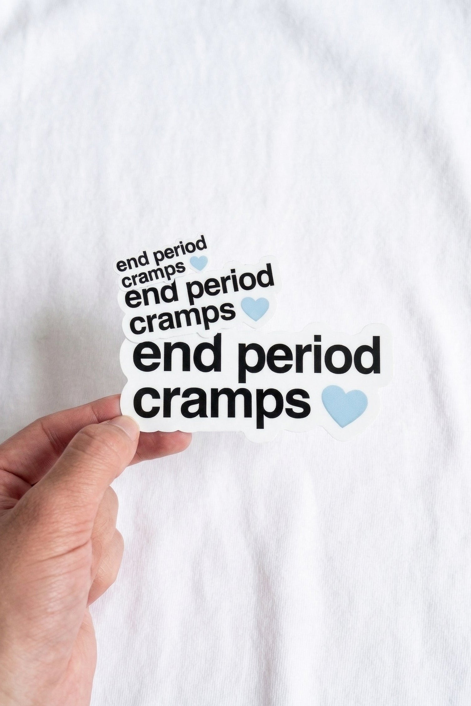Hand holding a sticker with 'end period cramps' text on a white background